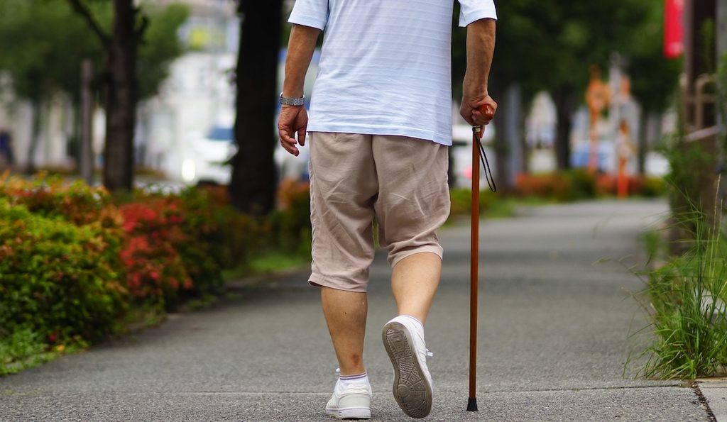 脳梗塞後のリハビリで杖をついて歩く男性