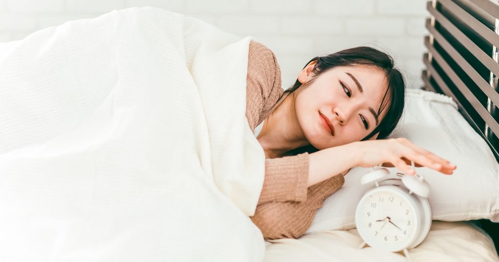 目覚まし時計をなん度もスヌーズする女性。
